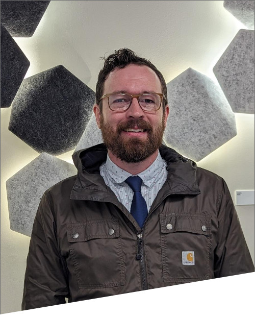 Man in coat standing against hexagonal wall art.