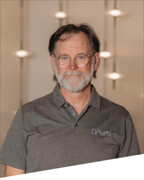 Man in gray DAVIS polo shirt smiling indoors.