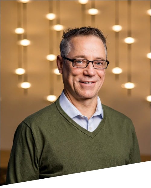 Smiling man in glasses with blurred lights background.
